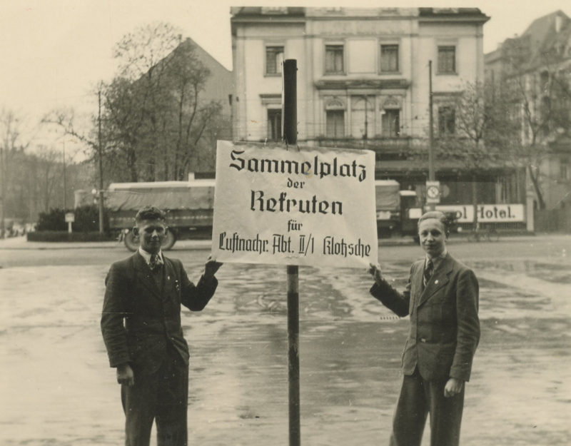 Two men standing next to a sign in the middle of an intersection.
