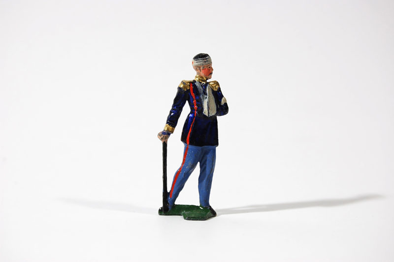 A toy soldier in uniform holding a cane and standing.