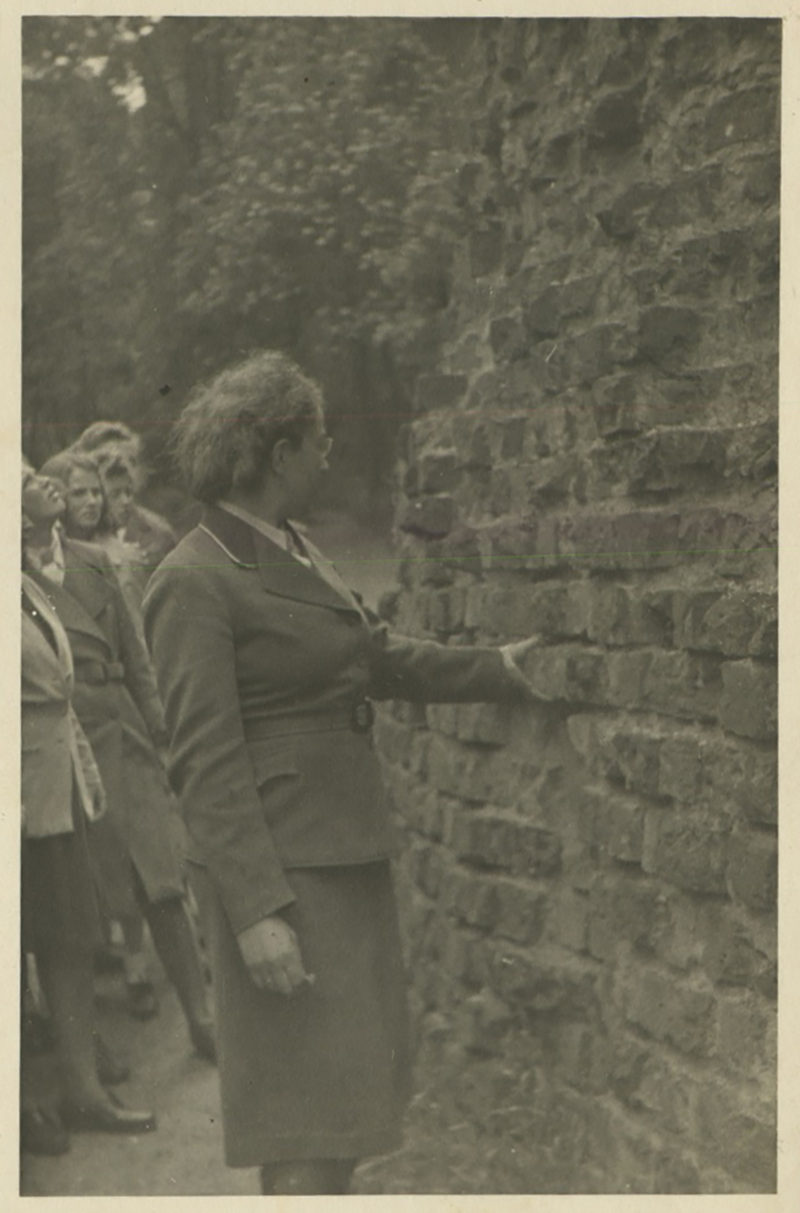 A woman in military uniform is leaning against the wall.